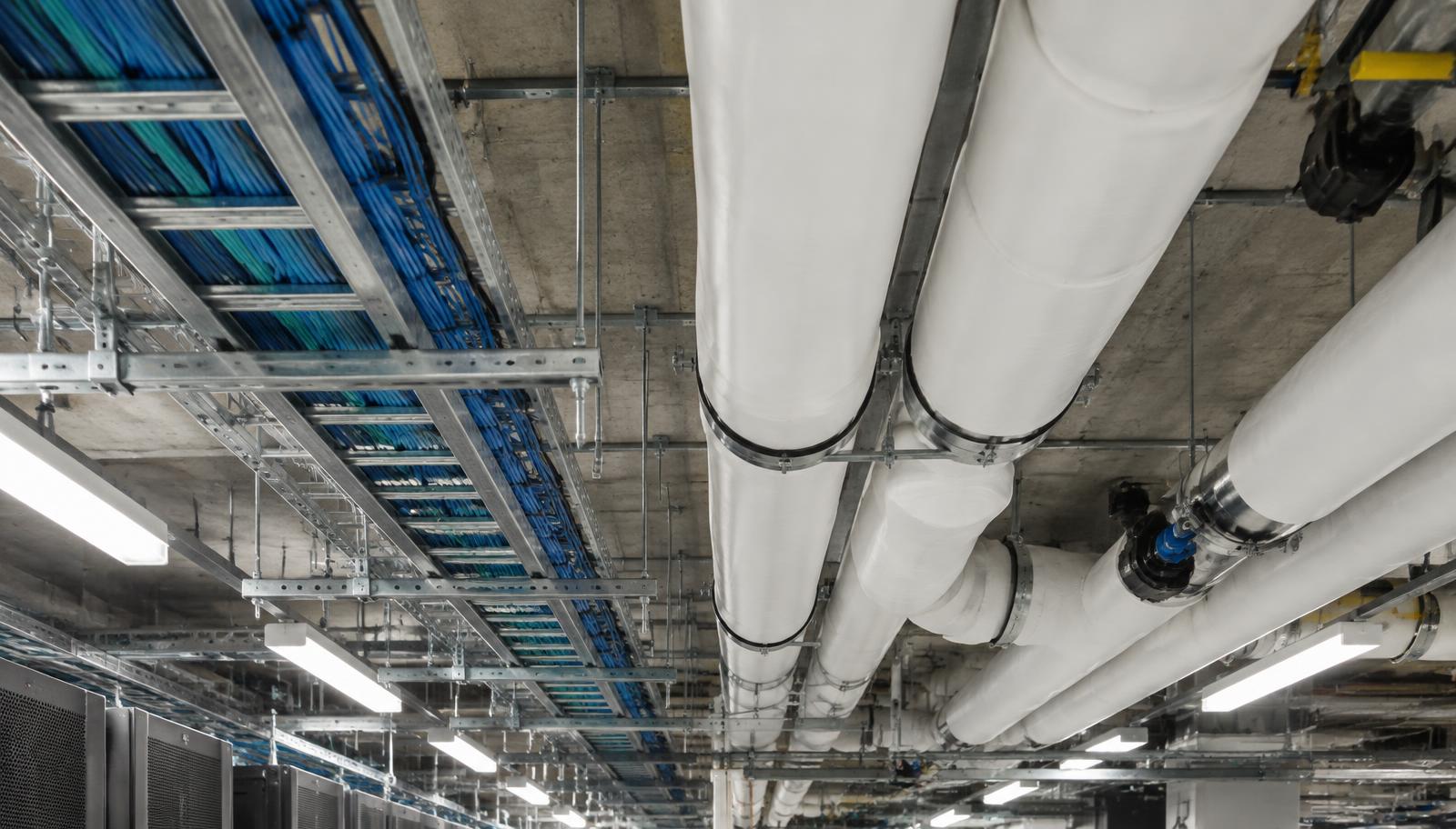 Overhead view of a data center plant room ceiling with insulated chilled water piping and cable tray running in parallel on coordinated hangers.